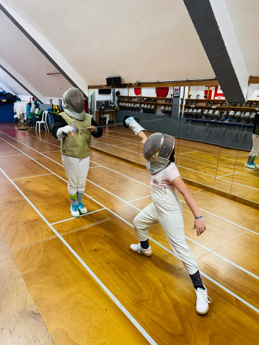 Dos niños practicando esgrima con careta frente a los espejos de la sala del club