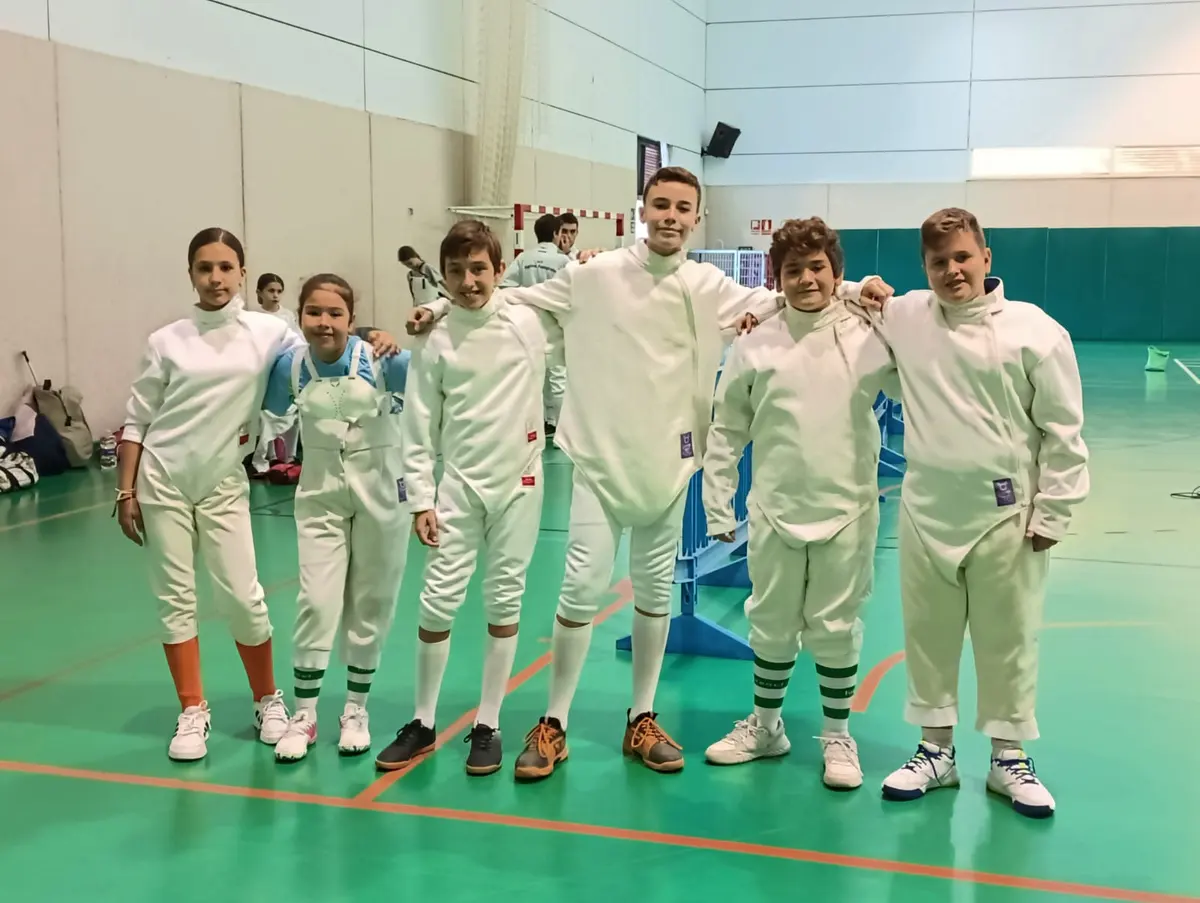 Seis niños y niñas esgrimistas posando juntos en un pabellón antes de competir