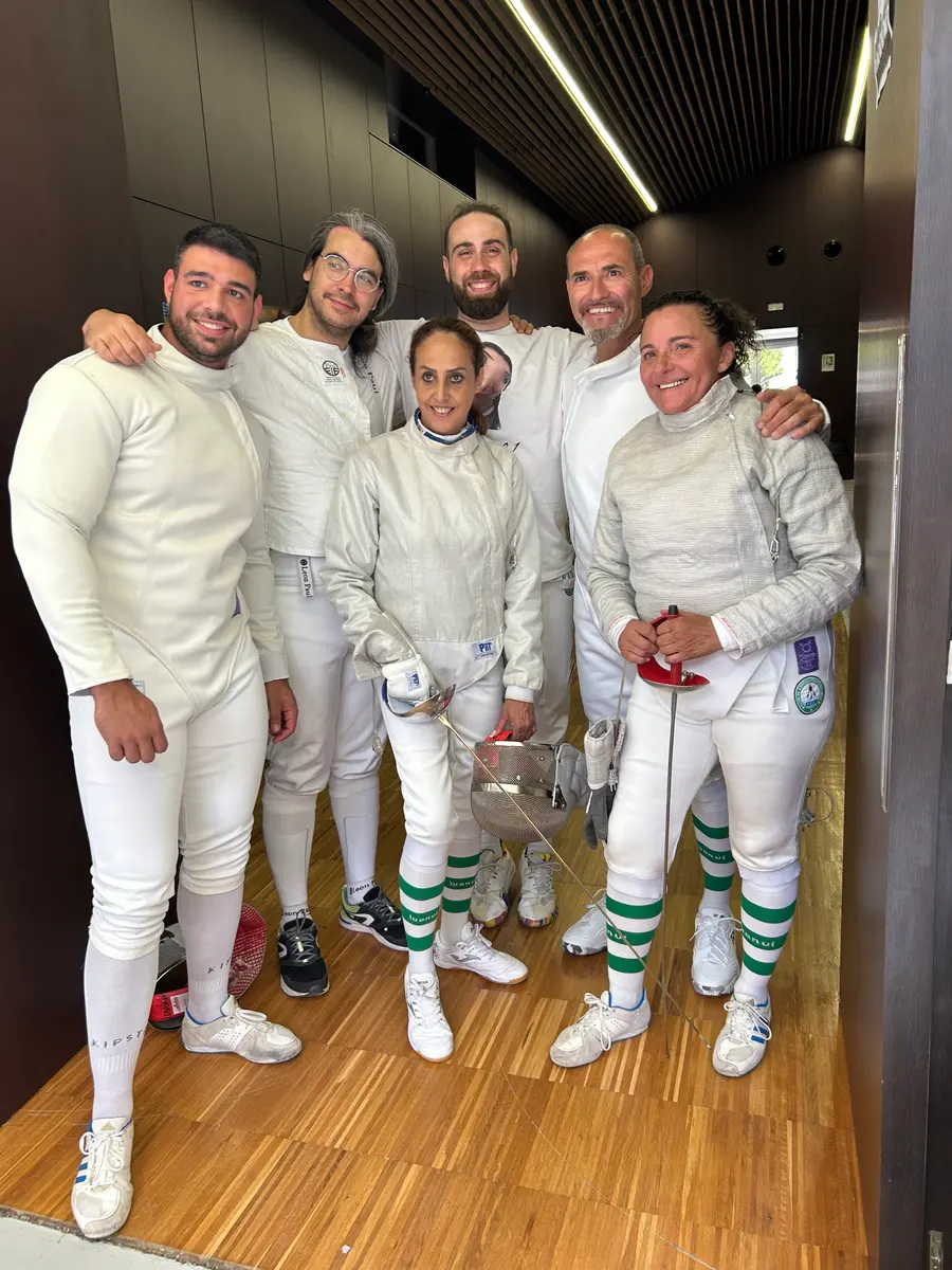 Seis esgrimistas adultos del club sonriendo juntos en un torneo