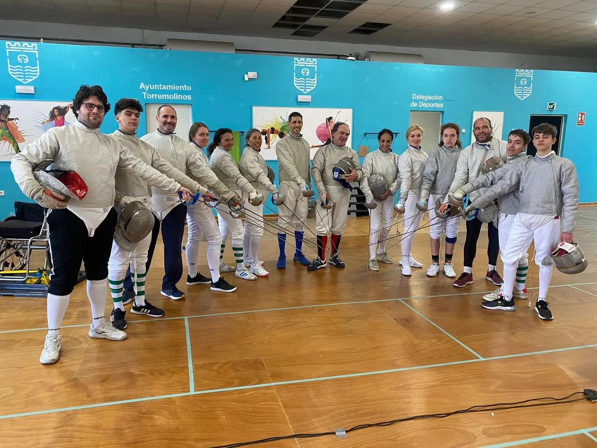 Grupo de esgrimistas de todas las edades haciendo el saludo con los sables en una sala de Torremolinos
