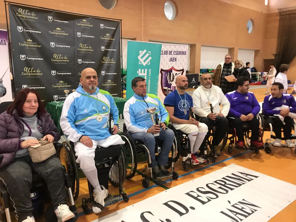 Esgrimistas en silla de ruedas con trofeos y medallas en el podio de un torneo en Jaén