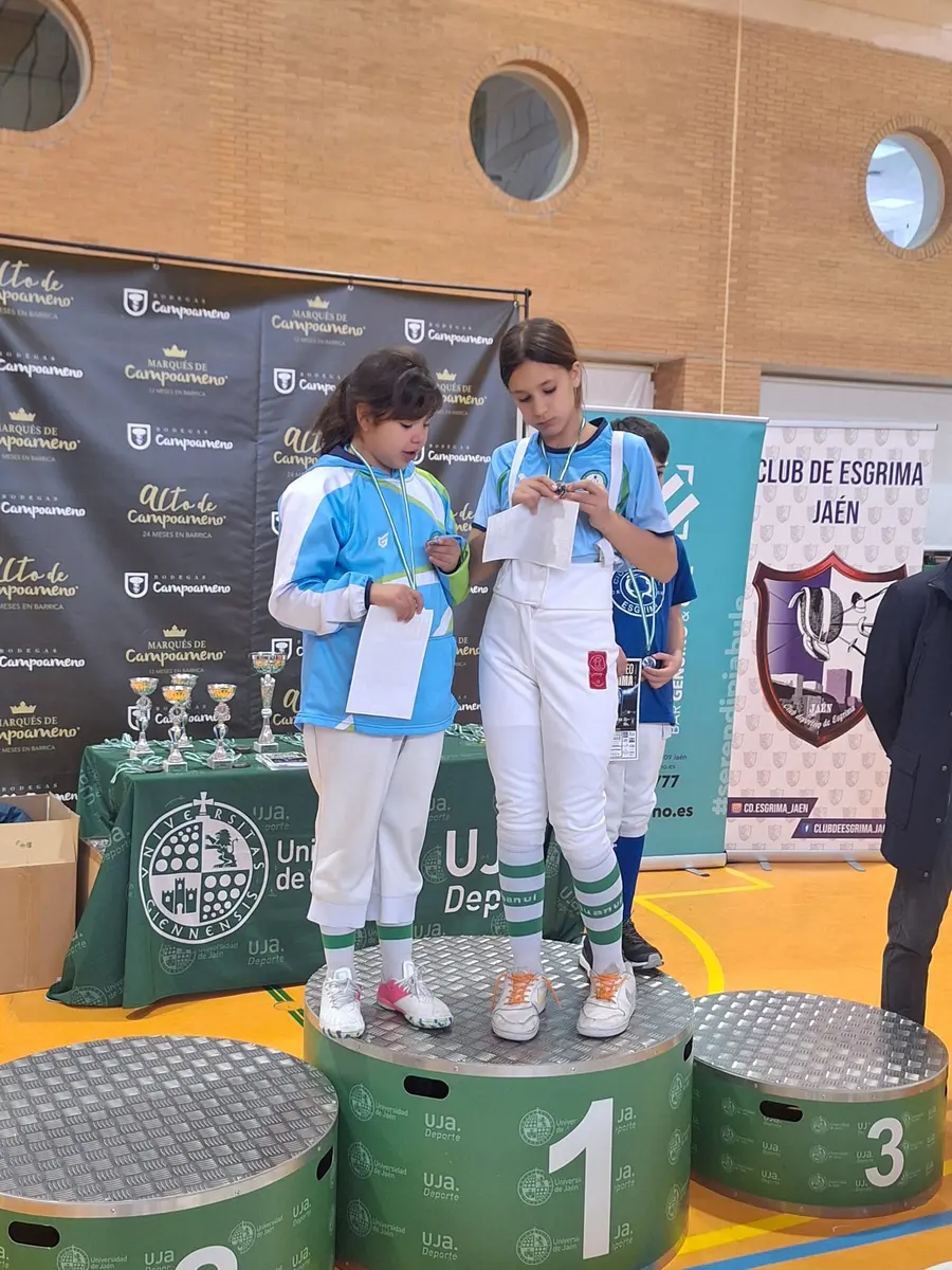 Dos niñas esgrimistas con su medalla sobre el podio de un torneo en Jaén